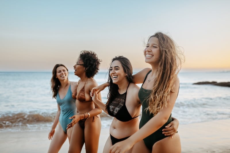 Joyful girlfriends in swimwear walking on beach