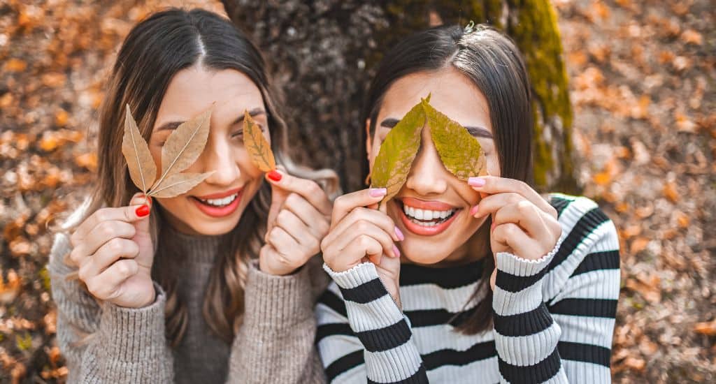 smiling women holding colorful leaves over eyes